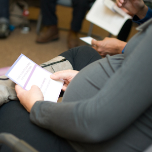 Close-up of two seated individuals holding pamphlets in an indoor setting.